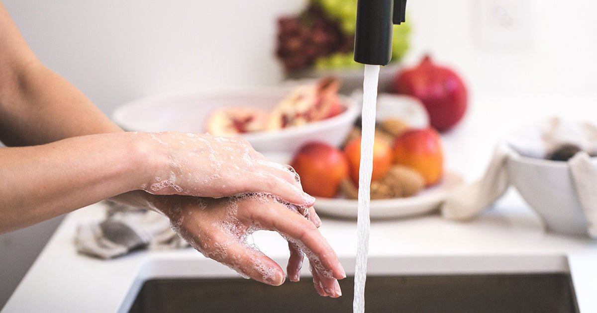 Woman washing hands over sink with produce in background