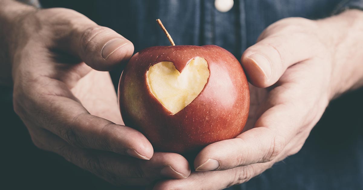 Man holding apple with heart carved into it