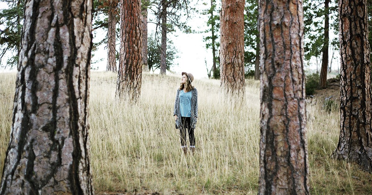 woman with hat standing in tall grass between trees