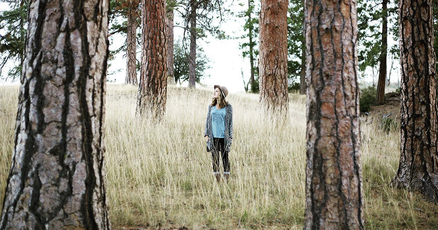 woman with hat standing in tall grass between trees