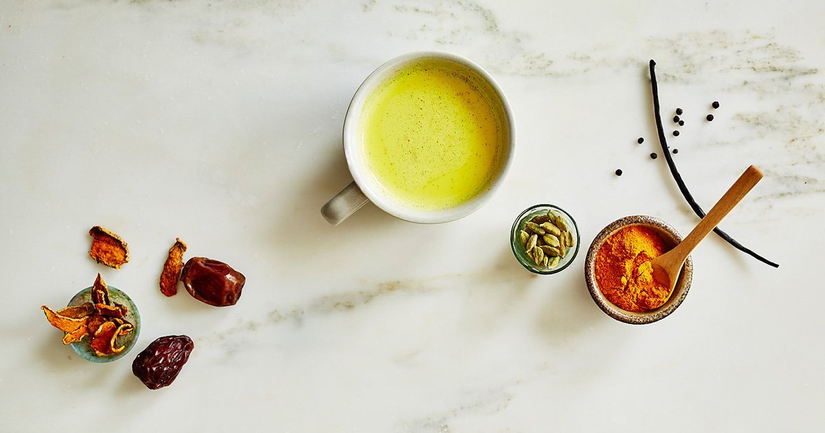 Golden Milk in mug surrounded by turmeric, dates, and herbs
