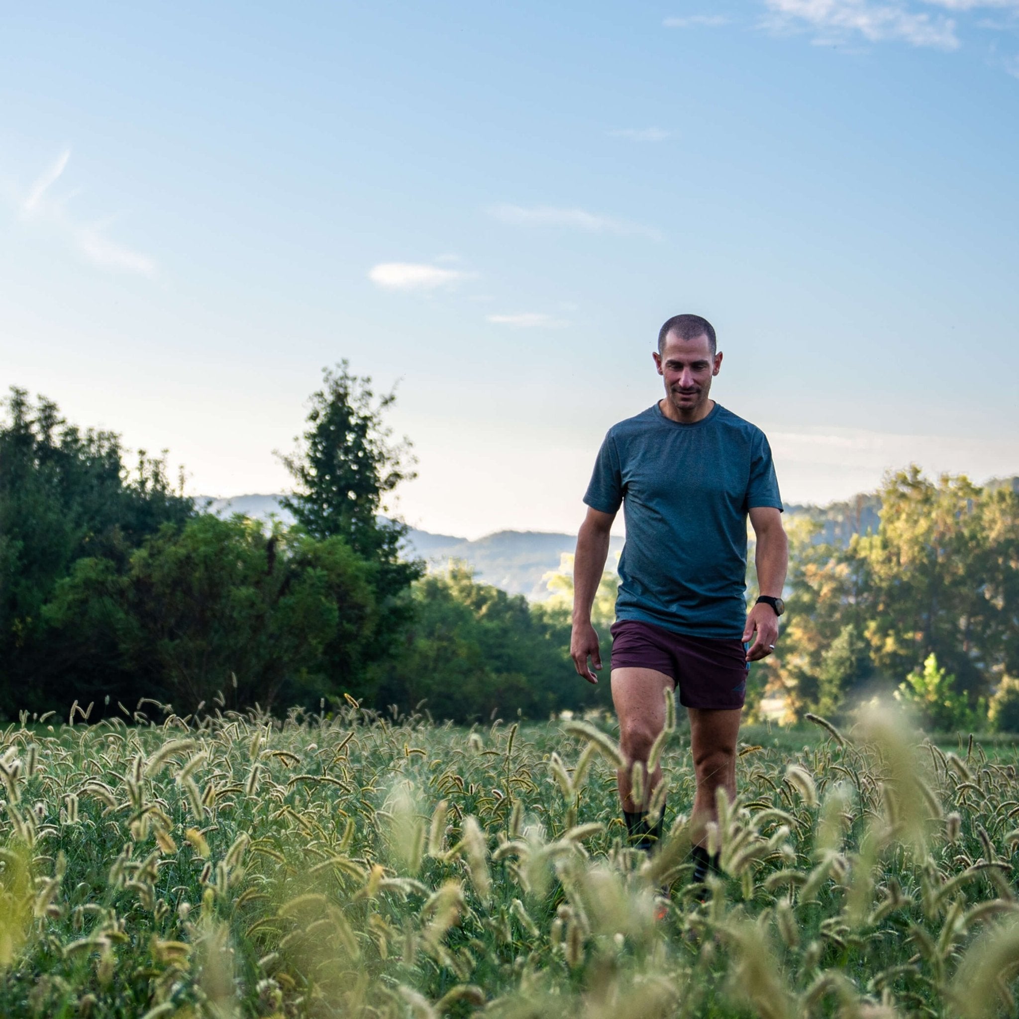 Man walking through a field with trees and mountains in the background