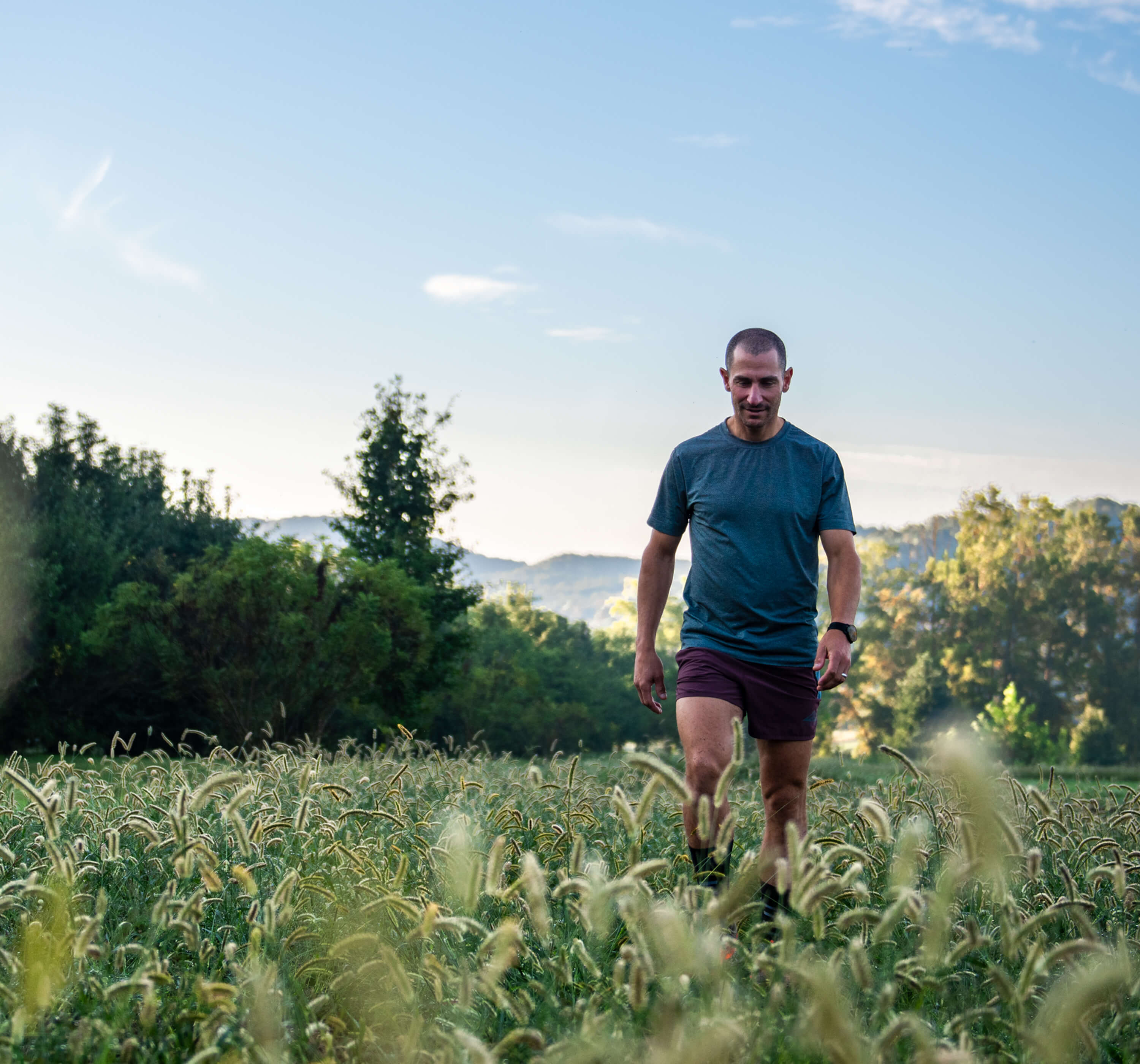 Man walking through a field with trees and mountains in the background