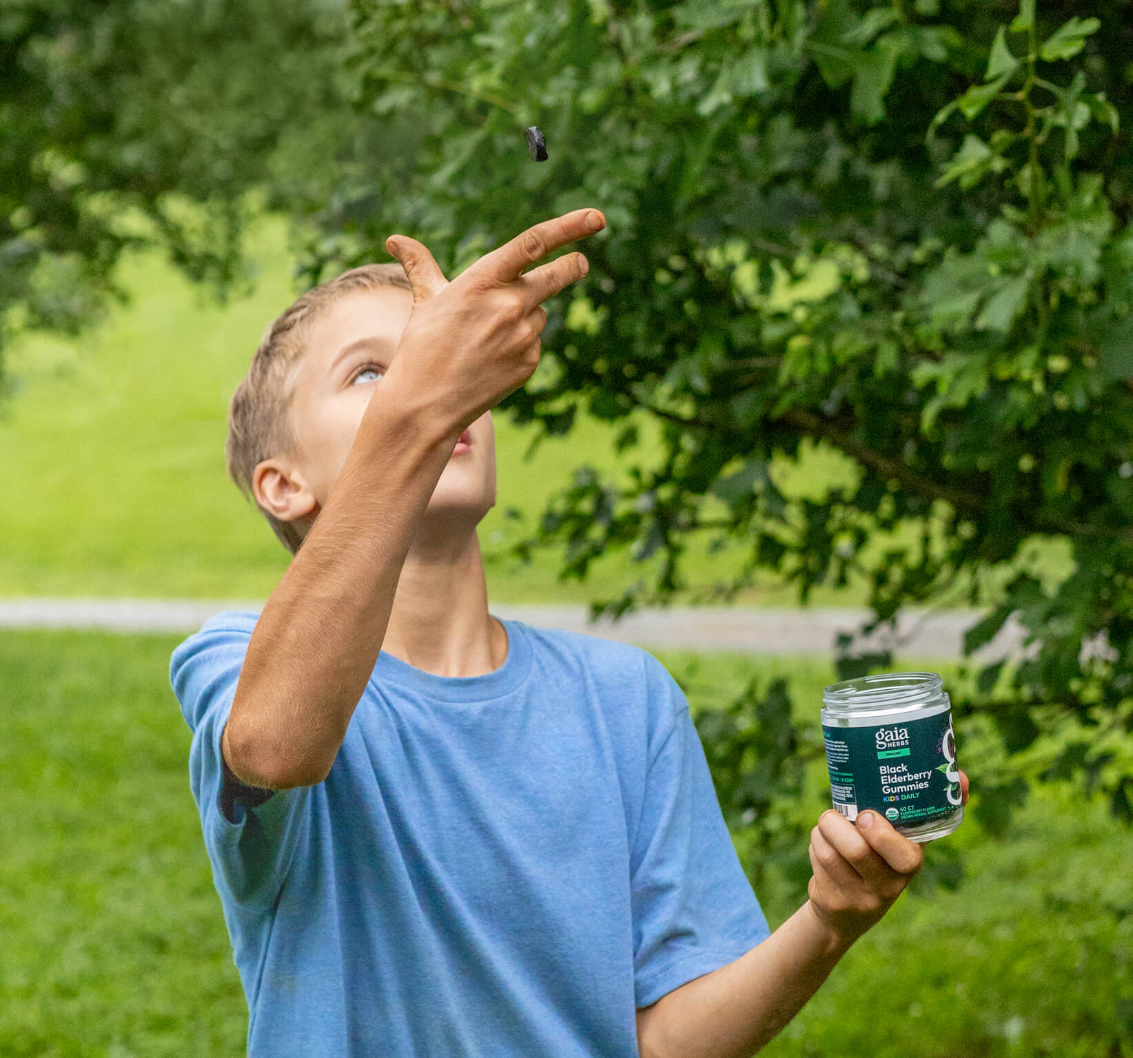 Boy in blue shirt holding a jar outdoors with greenery in the background