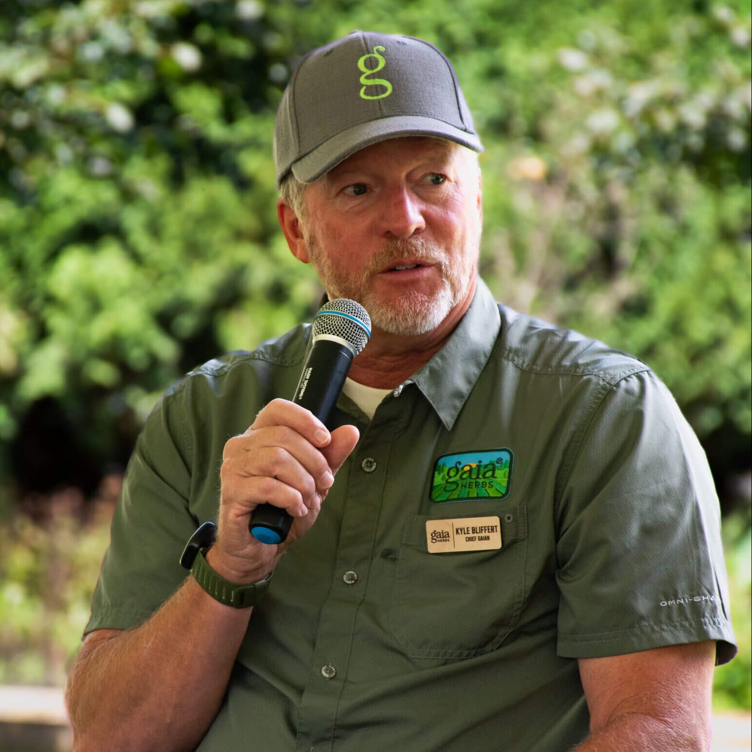 Kyle Bliffert, Gaia Herbs CEO speaking into a microphone outdoors for a Kiss the Ground event