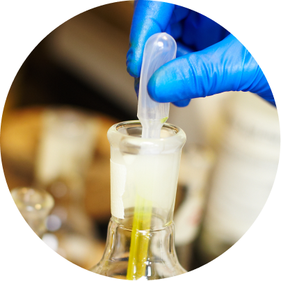 Hand in blue glove holding a pipette over a beaker with a blurred background