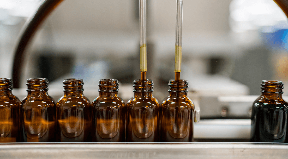 Row of brown glass bottles with droppers being filled in a laboratory setting